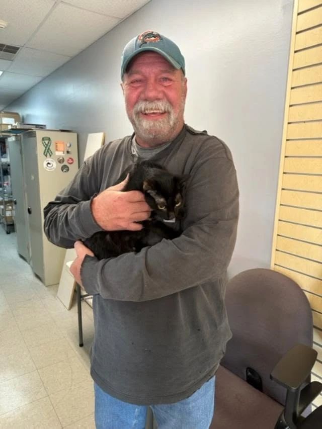 A smiling supporter cradling a black cat in the clinic hallway